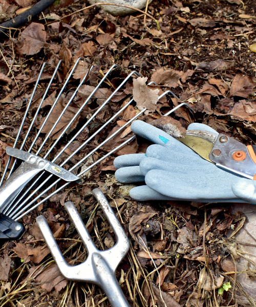 A pair of gardening gloves laying on the ground next to a pair of gardening tools